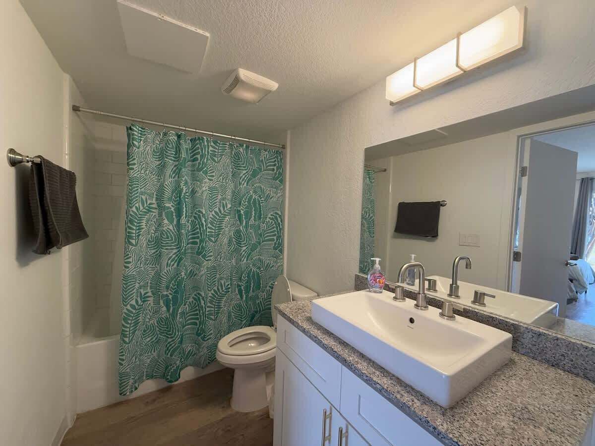 A bathroom with a shower curtain, toilet, sink, and mirror.