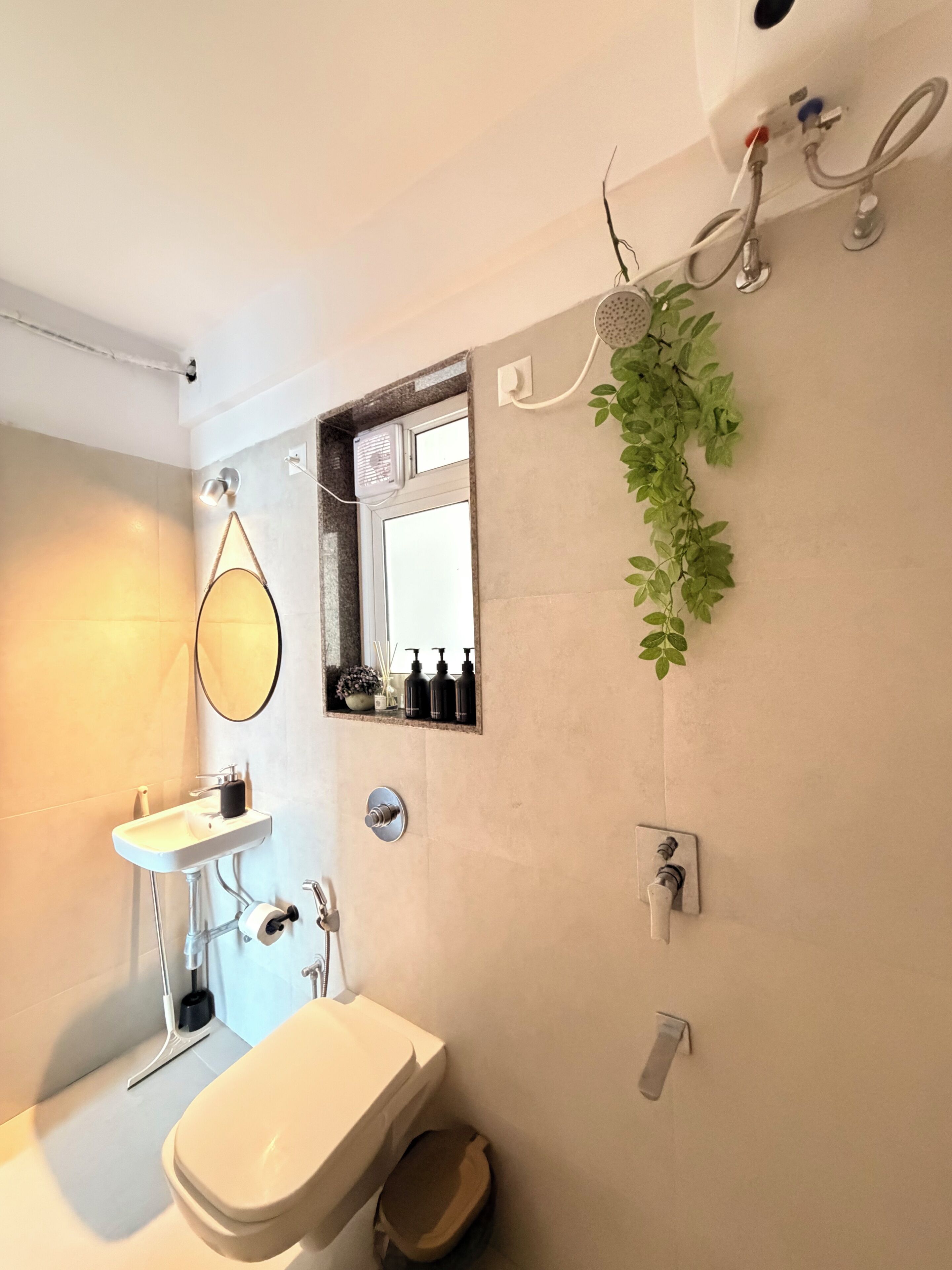 A bathroom with a sink, mirror, toilet, shower, and a plant.