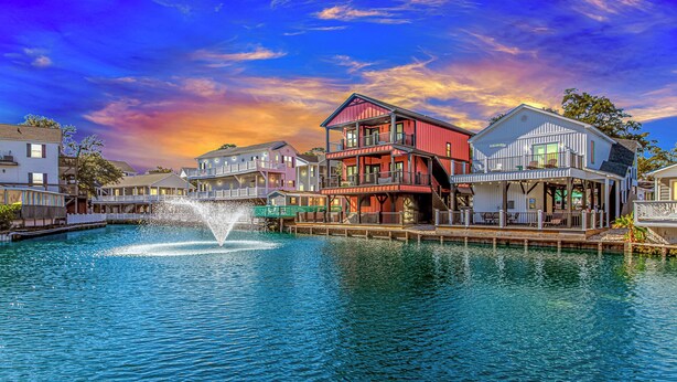 A waterfront property with a central building featuring multiple balconies and a dock extending into the water. - N125:  Lakefront 3br/2ba Home in Ocean Lakes - "Sandy Cove" (Myrtle Beach)