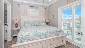A bedroom with a bed, bedside tables, a ceiling fan, a window with blinds, and a view of the city. - N125:  Lakefront 3br/2ba Home in Ocean Lakes - "Sandy Cove" (Myrtle Beach)