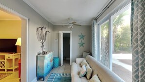 A living room with a sofa, a television, a ceiling fan, and a view of the outdoors. - Tidal Breezes (Tybee Island)