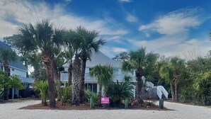 A beachfront property with a white building, palm trees, and a clear sky. - Tidal Breezes (Tybee Island)