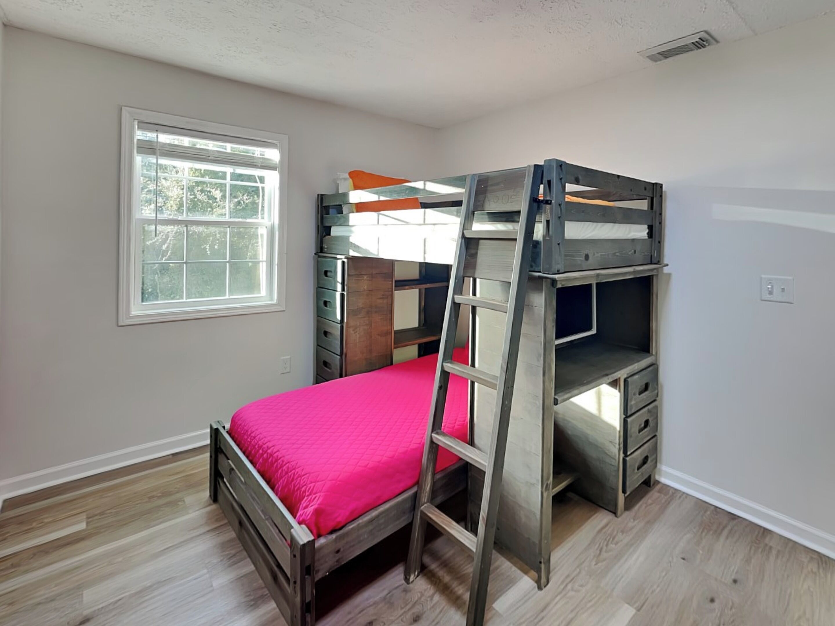 A bunk bed with a ladder, a window, and a dresser.