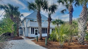 A two-story house with a gravel driveway, surrounded by palm trees and other vegetation. - Tidal Breezes (Tybee Island)