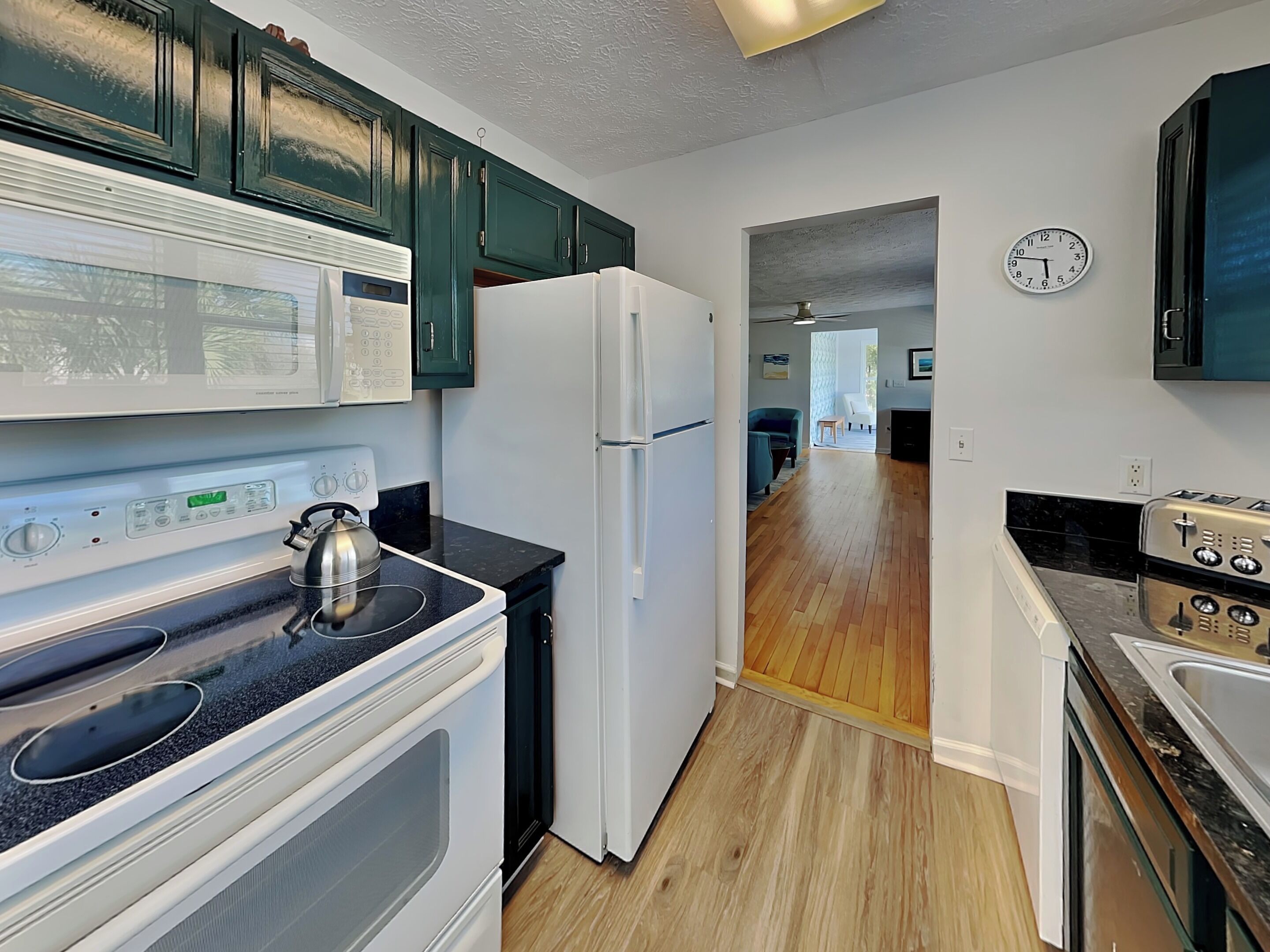 A modern kitchen with a microwave, stove, refrigerator, and a clock on the wall.