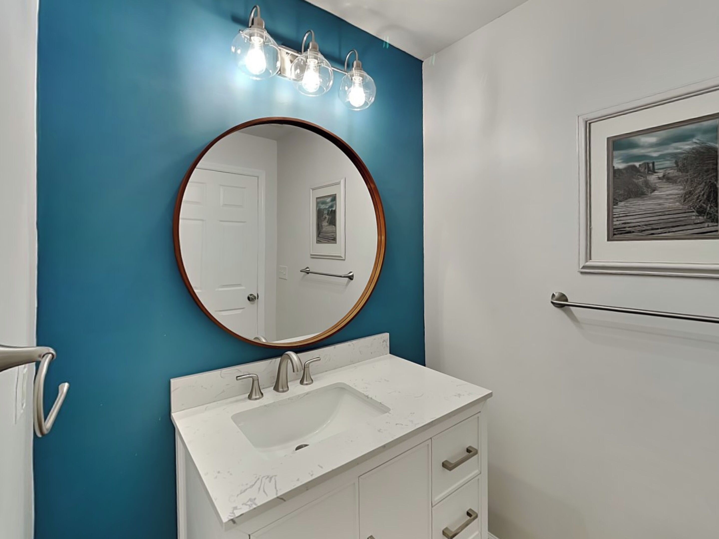A bathroom with a white sink, a round mirror, and a blue accent wall.