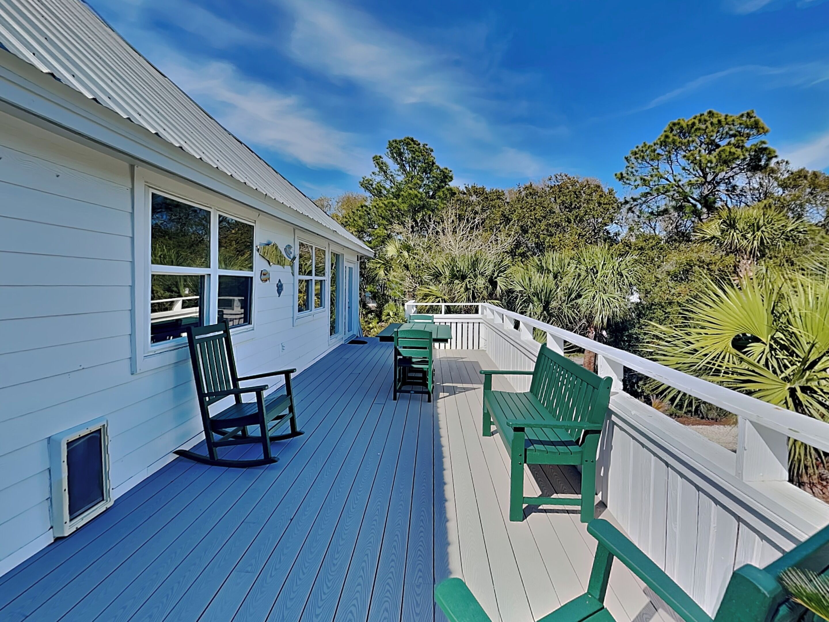 A white building with a wooden deck, green chairs, and a white railing.