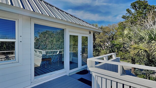 A house with a deck, large sliding glass doors, and a metal roof. - Tidal Breezes (Tybee Island)
