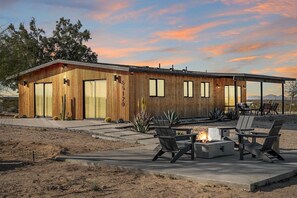 Un bâtiment moderne en bois, doté de grandes fenêtres, d’un patio avec des sièges extérieurs et d’un foyer.