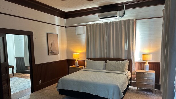 Ein Schlafzimmer mit einem Bett, zwei Nachttischen mit Lampen, einem Deckenventilator und einem Fenster mit Vorhängen.
