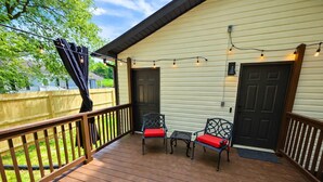 Eine überdachte Veranda mit Holzdeck, zwei Stühle mit roten Kissen, einem kleinen Tisch und Lichterketten.