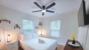 Ein Schlafzimmer mit einem Bett, Nachttischen, einem Deckenventilator und einem an der Wand befestigten Fernseher.