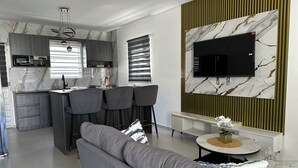 Un espacio habitable moderno con cocina, comedor y televisor montado sobre una pared de mármol.