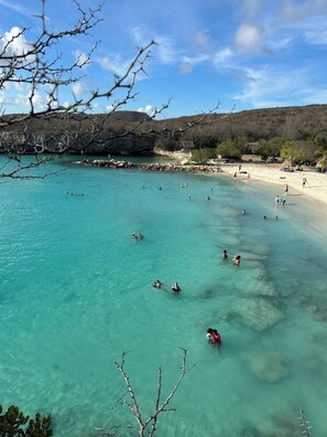 A beach with clear turquoise water, people swimming, and a rocky shoreline. - Villa Gomez Retreat - Private Pool & ModernComfort (Willemstad)