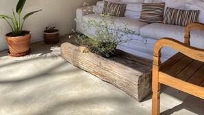 Et værelse med en hvid sofa, mange puder, en træstol og flere potteplanter.