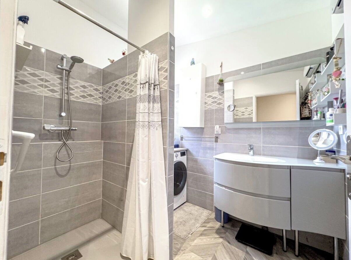 A modern bathroom with a shower, a washing machine, and a vanity with a mirror.