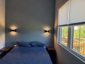 Un dormitorio con una cama, dos lámparas de pared, un ventanal con persianas y vista a una terraza.