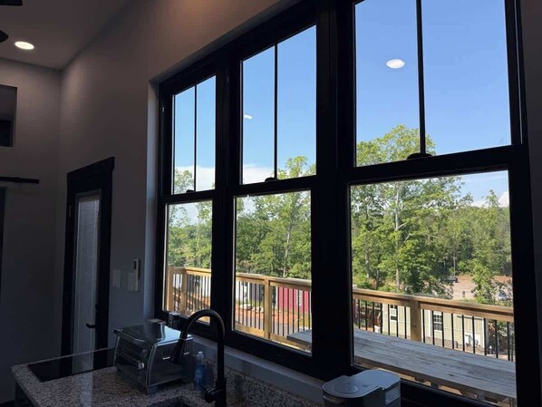 A room with large windows, a wooden deck, and a view of trees and a building. - Midnight Blue (Anderson)