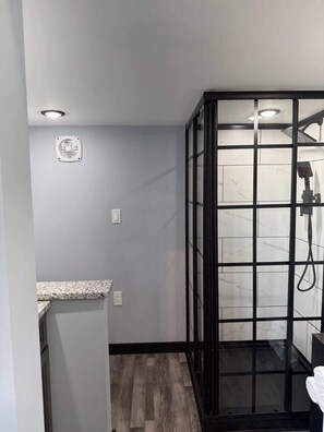 A modern bathroom with a shower enclosure, a granite countertop, and a marble-tiled shower area. - Midnight Blue (Anderson)