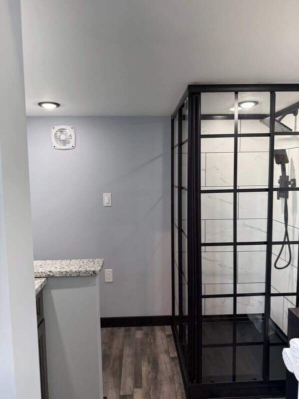 Une salle de bain moderne dotée d’une cabine de douche, d’un comptoir en granit et d’une zone de douche carrelée en marbre.