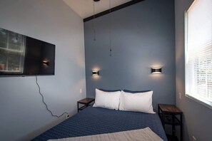 Un dormitorio con una cama, dos mesitas de noche, un televisor montado en la pared y dos apliques.