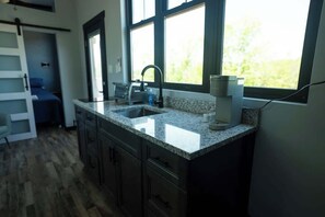 Una cocina con encimeras de granito, un lavamanos y una ventana con vistas a zonas verdes.