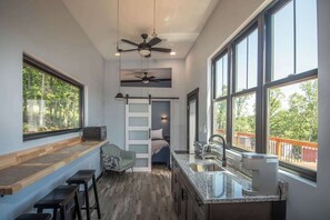 A modern kitchen with a built-in island, large windows, and a ceiling fan. - Midnight Blue (Anderson)