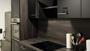 A modern kitchen with dark cabinetry, a built-in oven, a stainless steel refrigerator, and a Samsung dishwasher. - Modern 3 room apartment | subway fair | parking lot (Fürth)
