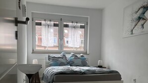 A modern bedroom with a bed, a floor lamp, and a window with curtains. - Modern 3 room apartment | subway fair | parking lot (Fürth)
