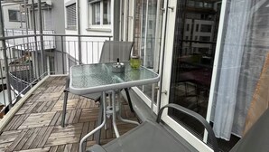 A balcony with a glass table and chairs, a metal railing, and a view of adjacent buildings. - Modern 3 room apartment | subway fair | parking lot (Fürth)
