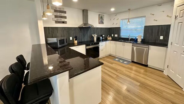 Een moderne keuken met een centraal eiland, witte kasten en een zwart aanrecht.