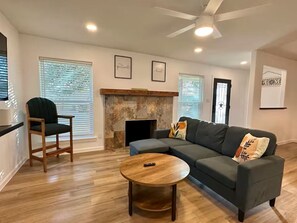 A living room with a sectional sofa, a round coffee table, a fireplace, and a ceiling fan. - Sleeps 6: Modern Family Home: Newly Remodeled (Richland Hills)