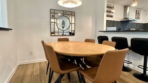 Een eetruimte met een ronde houten tafel en stoelen, een hanglamp en een keuken op de achtergrond.