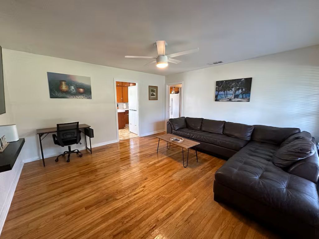 A living room with a dark brown leather sofa, a wooden coffee table, a black office chair, and a ceiling fan.