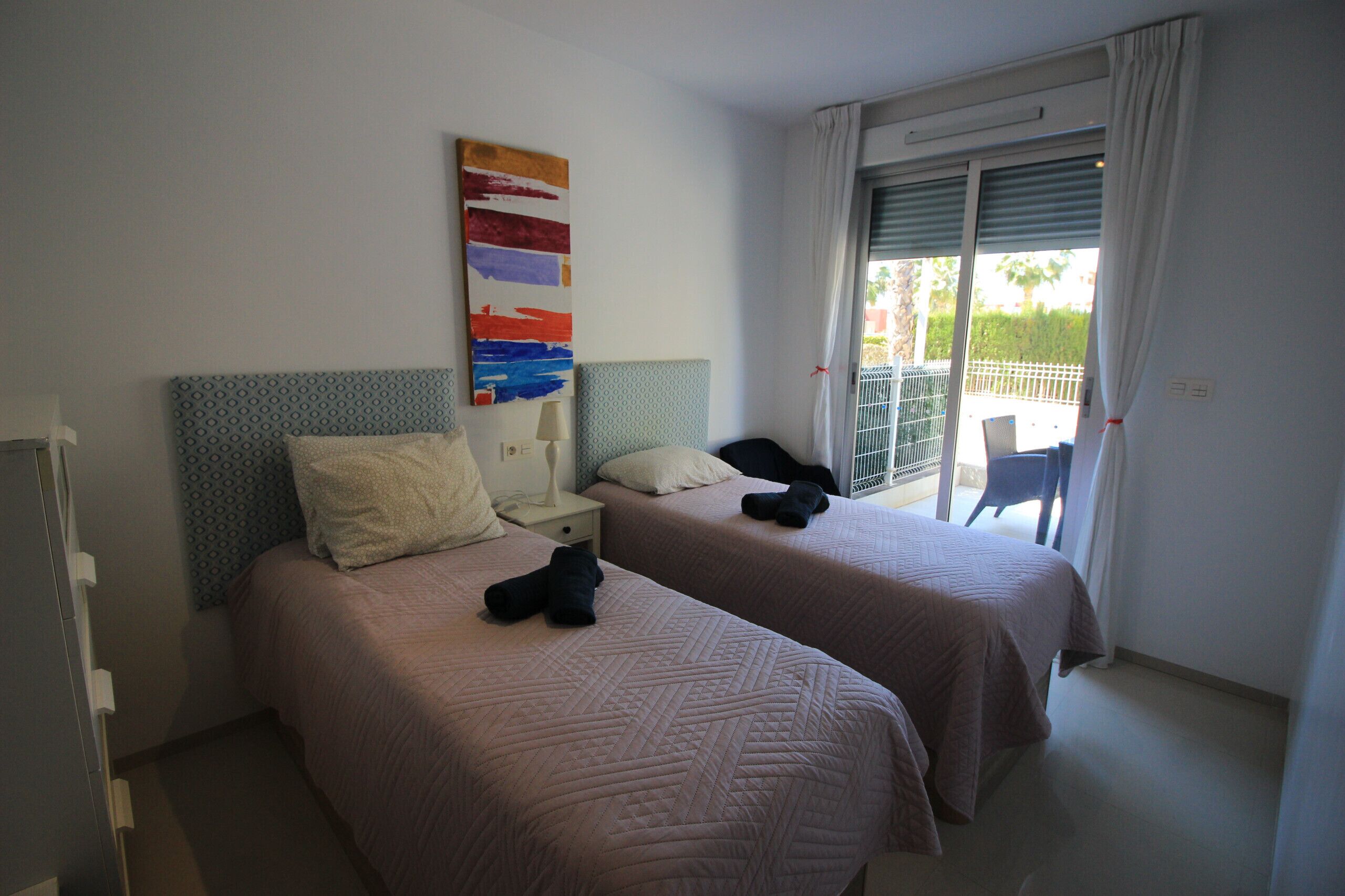 Une chambre d’hôtel avec deux lits, une table de chevet, une lampe, un tableau et une vue sur l’extérieur grâce à une porte coulissante.
