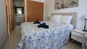 Una camera da letto con un letto, un comodino, una lampada, un quadro, un armadio e un bagno parzialmente visibile attraverso una porta aperta.