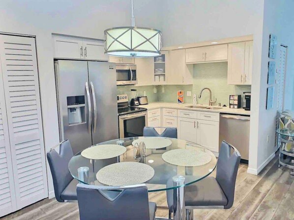 A modern kitchen with a glass dining table, stainless steel appliances, and light-colored cabinetry. - Near Beaches & IMG Academy, Mins to Downtown (Bradenton)