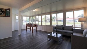 A spacious living room with a sofa, coffee table, and foosball table, large windows with a view of the outdoors. - Near Beaches & IMG Academy, Mins to Downtown (Bradenton)