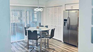 A modern kitchen with a stainless steel refrigerator, a dining table with chairs, and a glass-top coffee table. - Near Beaches & IMG Academy, Mins to Downtown (Bradenton)