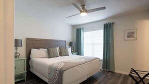 A bedroom with a bed, a ceiling fan, a nightstand, a lamp, a chair, and a window with curtains. - Near Beaches & IMG Academy, Mins to Downtown (Bradenton)