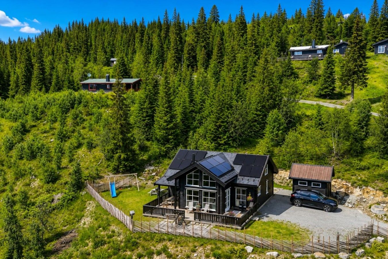 A modern house with a large deck, surrounded by a forested area.