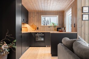A compact kitchen with a built-in oven, wooden cabinets, and a window with a view of trees.