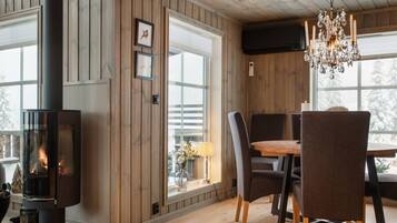 A room with a wood-paneled wall, a fireplace, a dining table with chairs, and a chandelier.