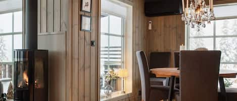 A room with a wood-paneled wall, a fireplace, a dining table with chairs, and a chandelier.