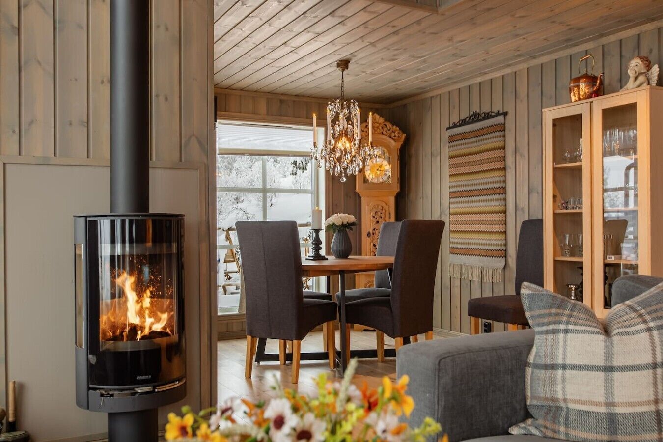 A cozy room with a wood-burning stove, a dining table with chairs, and a sofa with cushions.