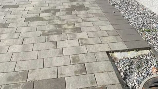 En belagt sti fører til en garage, omkranset af en lav mur og et lille haveområde.