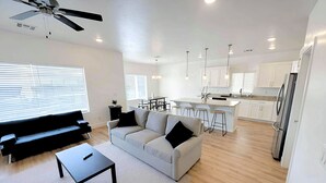 A modern living room with a sofa, coffee table, and a dining area with a kitchen in the background. - Spacious 4BR in Red Trails 30+ Day Stays (Washington)