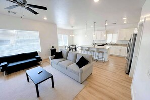 Een moderne woonkamer met een bank, salontafel en een eethoek, met een keuken op de achtergrond.