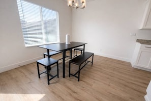 A room with a dining table and benches, a window with blinds, a chandelier, and wooden flooring. - Monthly Stay | Southern Utah Escape (Washington)