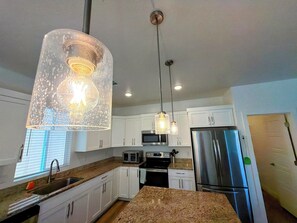 Een moderne keuken met witte kasten, roestvrijstalen apparatuur, granieten werkbladen en hanglampen.